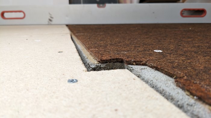 En närbild av ett skadat brunaktigt golv med en vågig vattenpass i förgrunden.