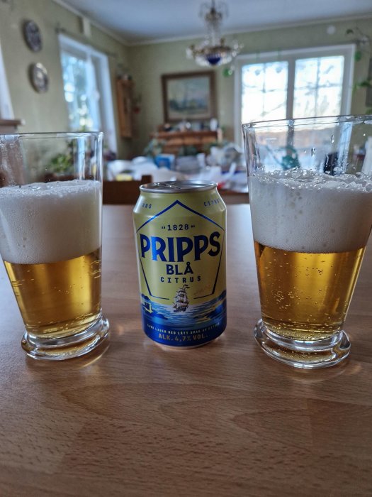 Två glas öl och en burk Pripps Blå Citrus på ett bord i ett hemtrevligt kök.