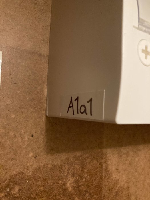 Etikett med text "A1a1" på en vit yta, skugga, närbild, brunt underlag.