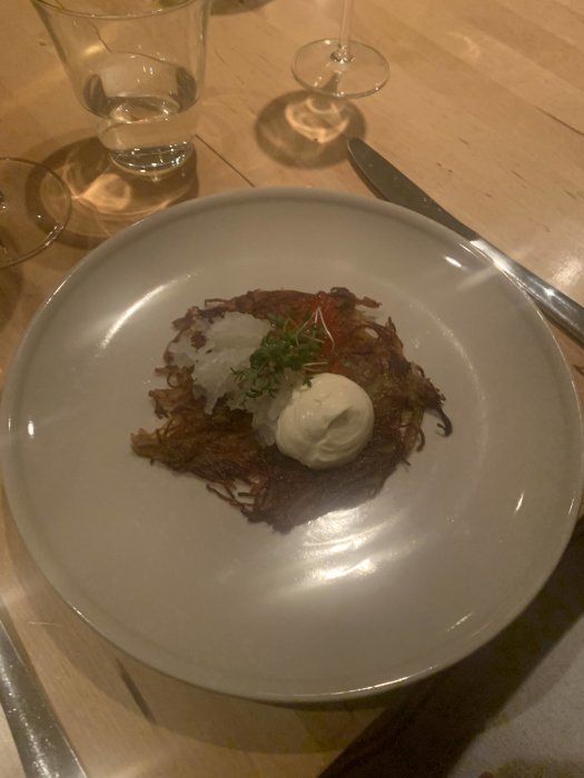 Ett fat med mat: rostade potatisstrån, crème fraîche, löjrom. Glas och kniv syns; mysig restaurangmiljö.