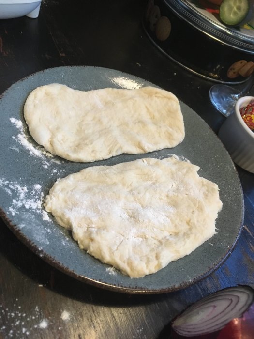 Två formade degbitar på en tallrik, redo för gräddning eller bakning, mjöldammade, hantverksmässigt bakverk.