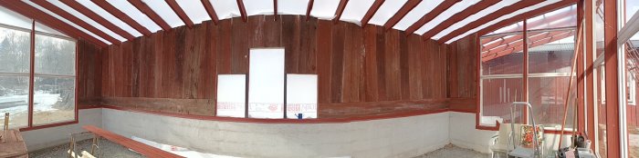 Panoramavy av en halvfärdig inglasad veranda med röda väggar och vit-grå grund. Byggmaterial och redskap synliga.