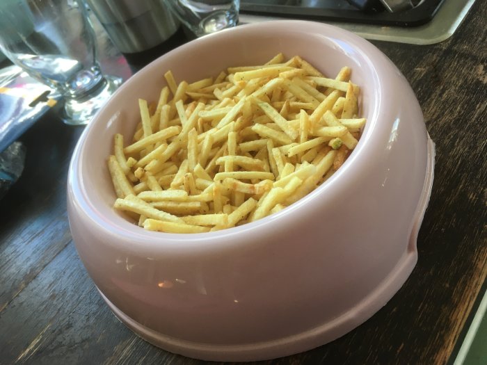 En rosa skål fylld med gyllene pommes frites på ett träbord.