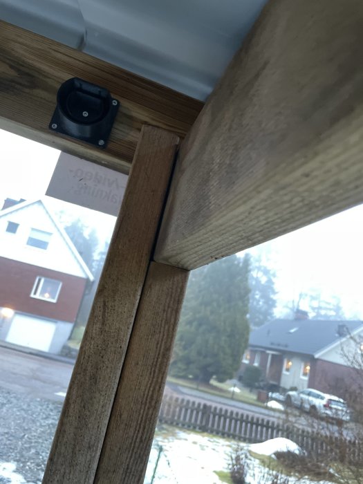 Trähörn med svart högtalare, suddig utsikt på hus och trädgård genom fönster, dagsljus, snöfläckar utomhus.