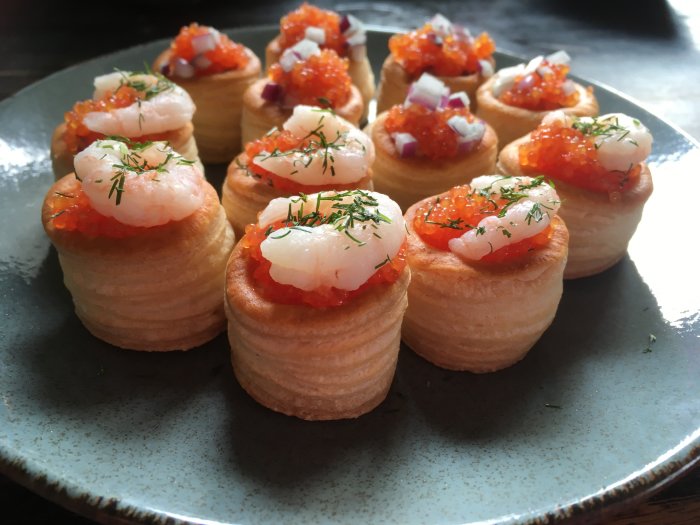 Vol-au-vent aptitretare med räkor, löjrom, rödlök, dill på mörk tallrik.