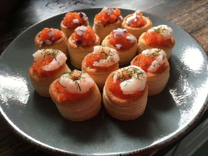 Festliga snittar med löjrom, räkor, rödlök och dill på en tallrik.