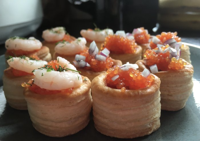 Vol-au-vent aptitretare med löjrom, räkor, rödlök och dill på serveringsfat.