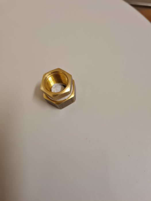 Guldfärgad sexkantig metallmutter med gängor på en vit yta.