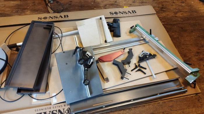 Delar och verktyg på bord, möjigtvis för CNC-maskin eller 3D-skrivare, i rörig ordning.