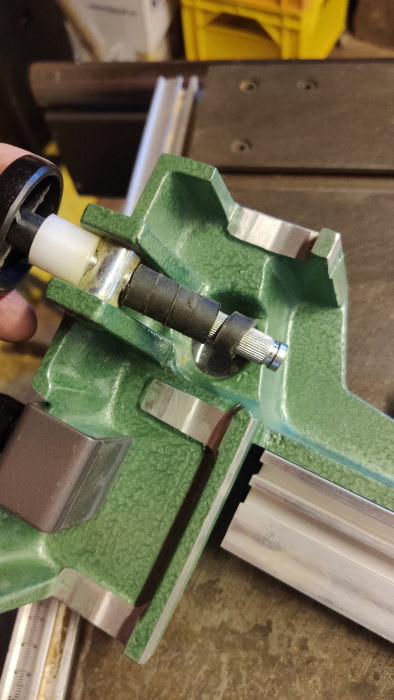 Hand håller verktyg som klämmer ett rör, troligen för underhåll eller reparation, i en verkstad.