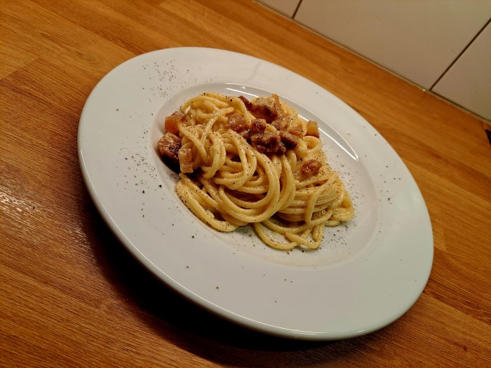 Ett fat spaghetti med köttbitar och peppar, snyggt presenterat på en vit tallrik.