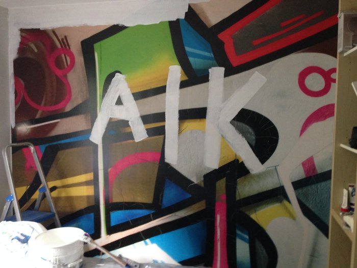 Stor målning med bokstäverna AIK, färgstark grafitti-stil, konstnärlig, pågående arbete, stege, målarutrustning.