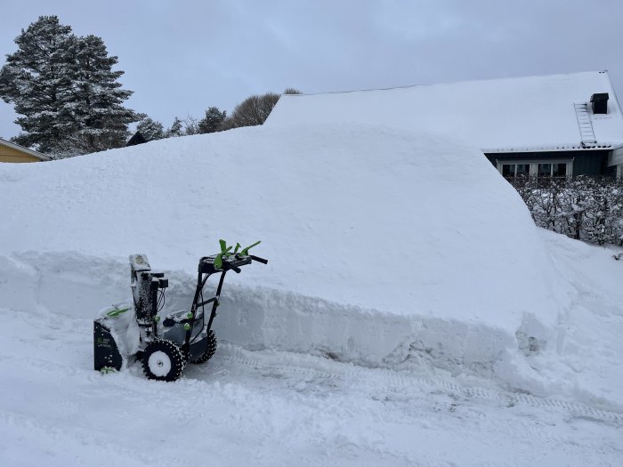 Snöslunga framför hög snövägg, vinterlandskap, hus delvis dolt av snön.