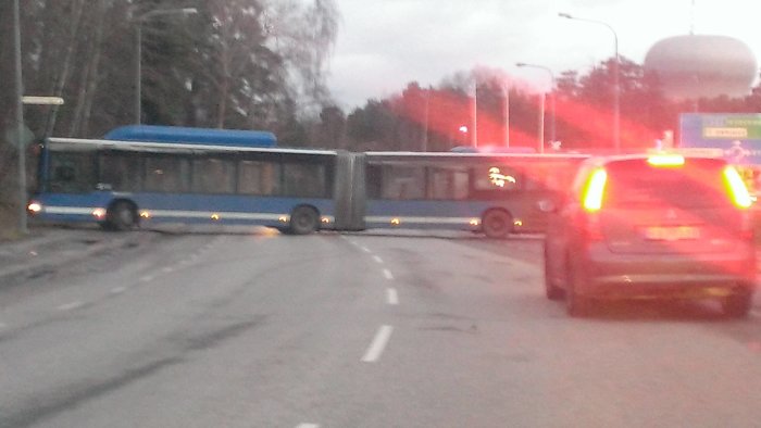 En otydlig bild av en ledbuss som svänger på en gata, trafik, skymning, bakljus, stadsmiljö.