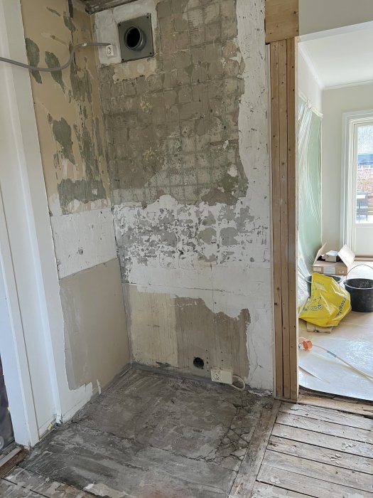 Renoveringsprojekt, nakna väggar, exponerad tegelsten, kabeldragning, trägolv, byggdamm, avlägsnade plattor, öppen dörr.