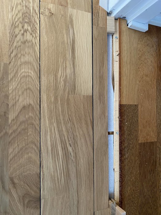 Delvis lagt trägolv bredvid äldre golv, synlig isolering, pågående renovering eller installation.