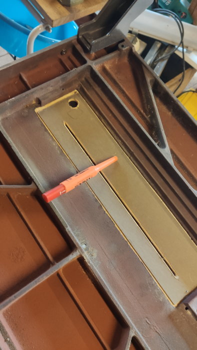 En röd märkpenna på ett brunaktigt metallbord med sågspår i verkstads miljö.