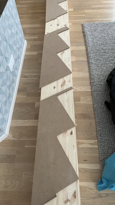 MDF-träbitar ligger i rad på trägolv bredvid matta och möbel.