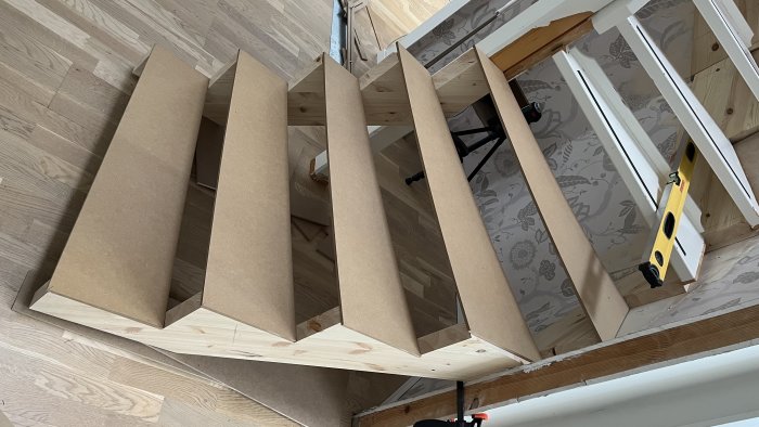 Träkonstruktion under uppbyggnad, brunt, trägolv, verktyg synliga, målningsarbete, omvänd perspektiv.