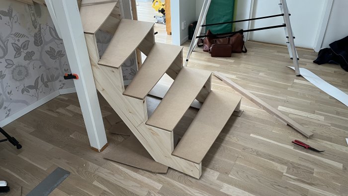 Trappa under byggnation i rum med verktyg och stege synliga.