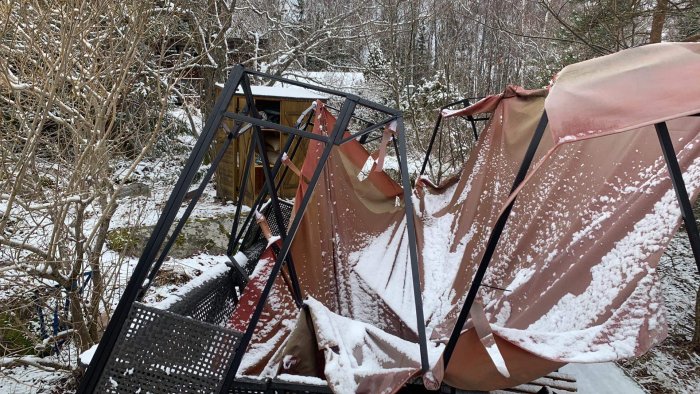 Förstörd paviljong under snötäcke i en trädgård, vinterns skadegörelse.