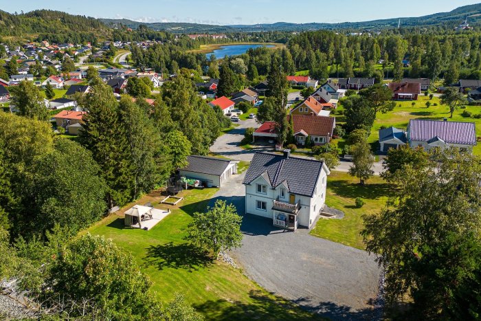 Luftvy av ett lugnt bostadsområde med enskilda hus, gröna trädgårdar och en sjö i bakgrunden.