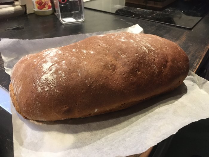 Nybakat bröd på bakplåtspapper, hemgjort, brun yta, mjöl på toppen.