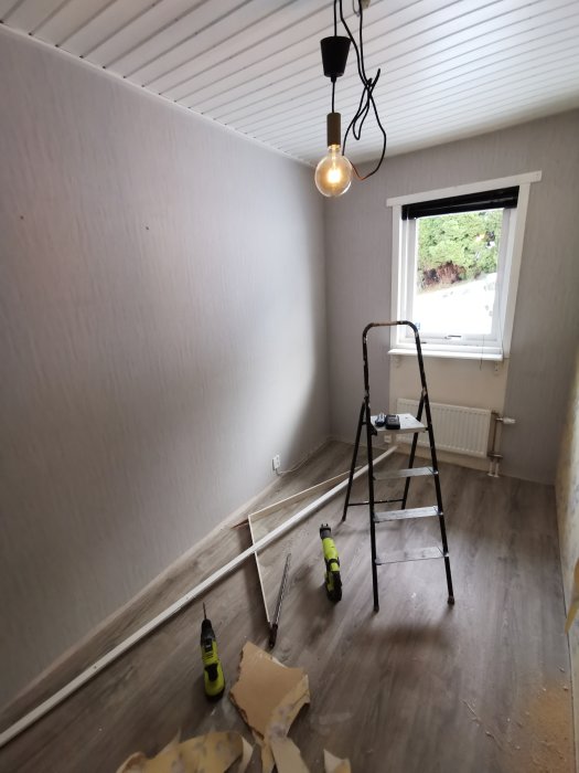 Tomt rum under renovering, stegar, nedrivet tapet, verktyg och trägolv.