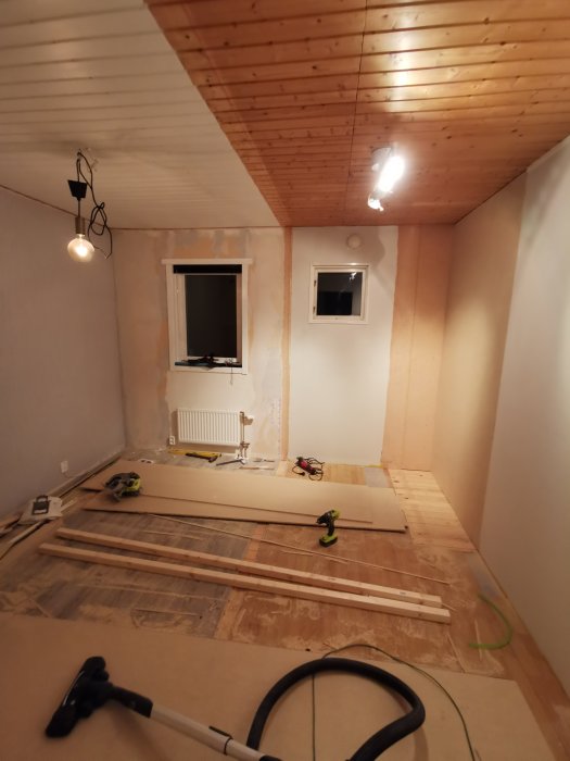 Ett under-renovering rum med trälisttak, spacklade väggar, och byggmaterial och verktyg på golvet.