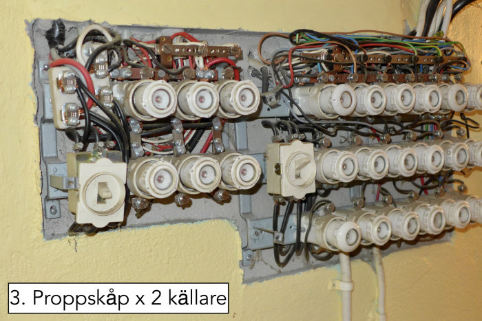 Ett gammalt proppskåp med säkringar och kablar syns i en källarmiljö, elektrisk distribution.