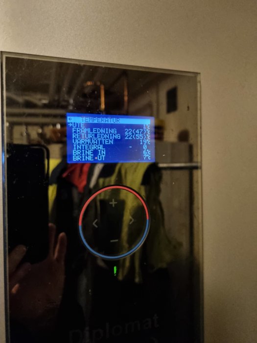 Digital termostat visar temperaturer. Speglad reflektion av en person som fotograferar. Inomhusmiljö. Regelteknik eller värmesystem.