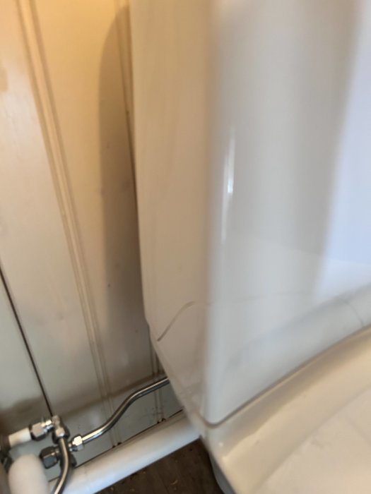 Badrumshörna med vit badkarssarg och synliga rörledningar, suddig bild med naturligt ljus.