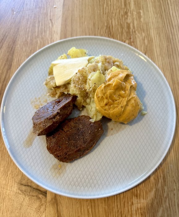 Ett matfat med potatismos, smörklick, vegobiffar och senap på ett träbord.