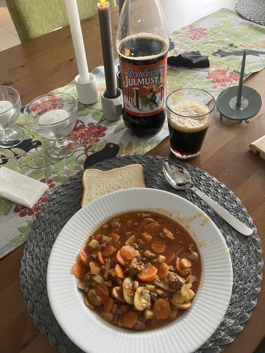 Gryta med nötkött, morötter, champinjoner, "Julmust" läskedryck, ljus, dukat matbord, brödskiva.