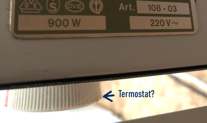 Etikett på elektronisk enhet, 900W, 220V, frågetecken indikerar okänd funktion, blå pil pekar.