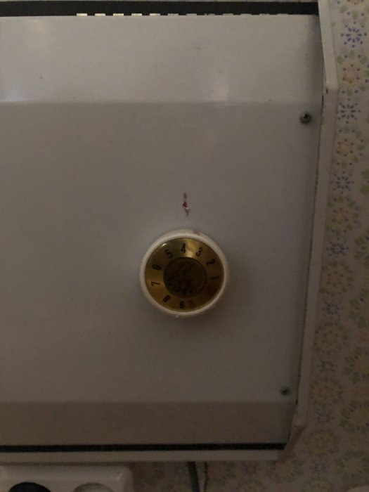 Analog termostat på vit enhet, gult skal, skala från 5 till 30, mörk omgivning.