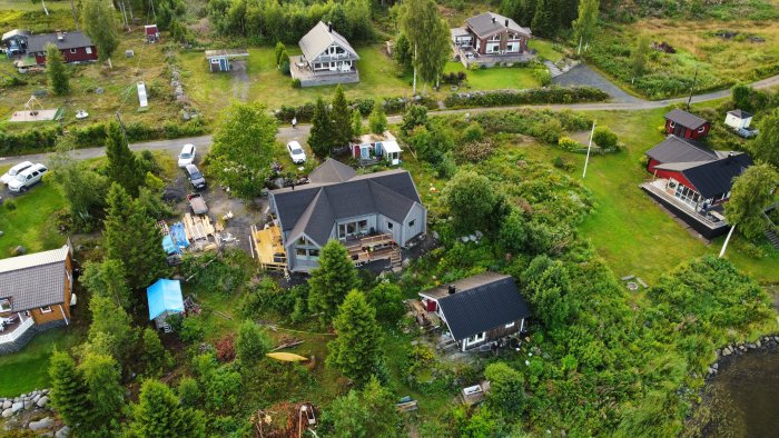 Flygbild av bostadsområde med hus, trädgårdar och bilar i lummig, grönskande miljö.