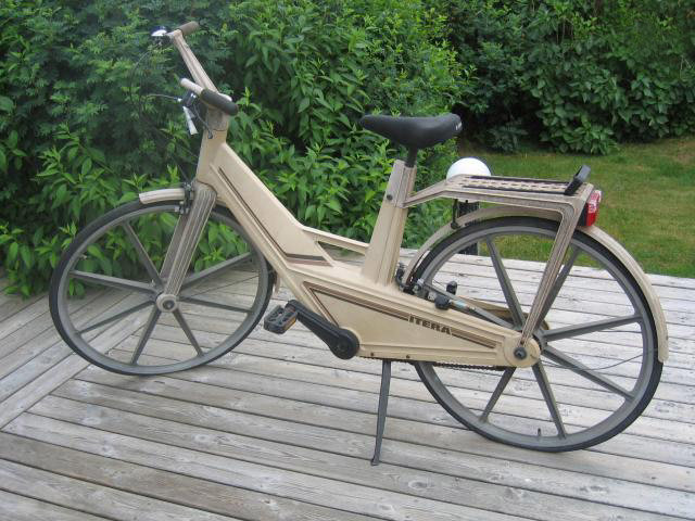 Beige plastcykel på träaltan, innovativ design, saknar typiska cykeldetaljer, verkar robust och väderbeständig.