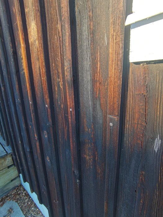 Vertikala bruna träbrädor, slitet staket, skuggor, solljus, utomhus, dagtid, närbild.