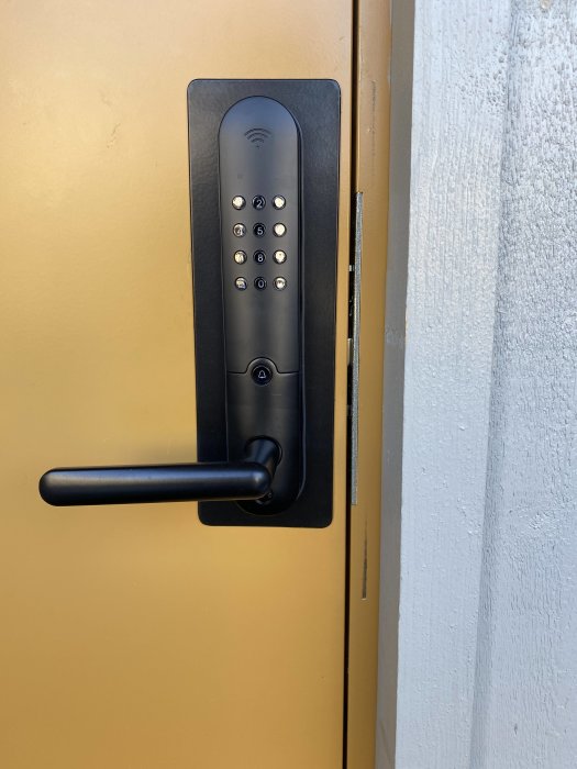 Digitalt lås med kodpanel och handtag på gul dörr, trådlös signalikon, modern säkerhetsteknik.