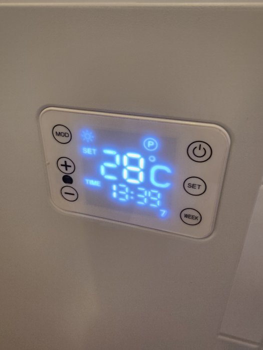 Digital termostat visar 28 grader Celsius, tidsinställning aktiverad, varm hus Komfort, väggmonterad, modern uppvärmningskontroll.