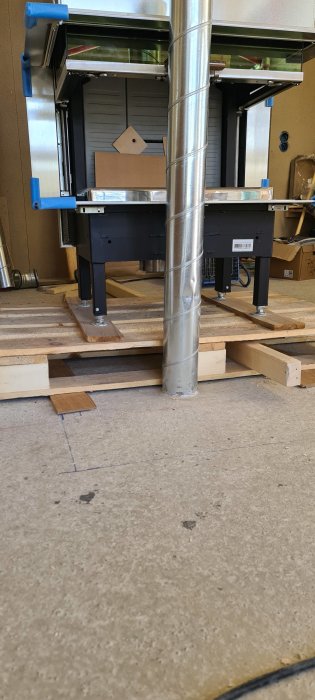 Verkstadsinredning med pallar och ventilation, två arbetsstationer syns, kabel kanaler på golvet.