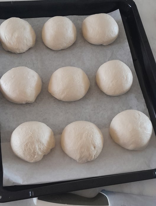 Åtta omjästa degklumpar upplagda på bakplåtspapper, förberedda för bakning.