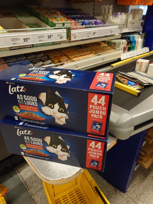 Storpack kattmat, kattbild, butikshyllor med varor, gula kundkorgar, avställningsyta.