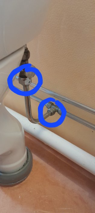 Toalettpappershållare, rörkopplingar markerade med blå cirklar, kakelvägg, brunt golv.