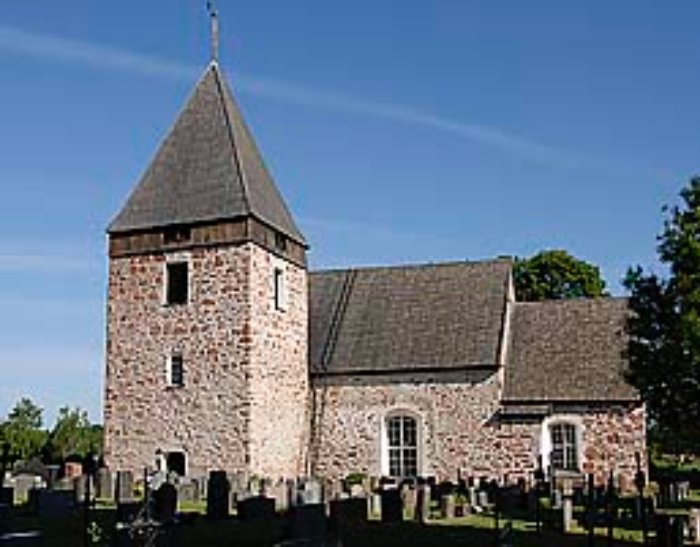 Gammal kyrka av sten med torn, kyrkogård, klart väder, blå himmel.