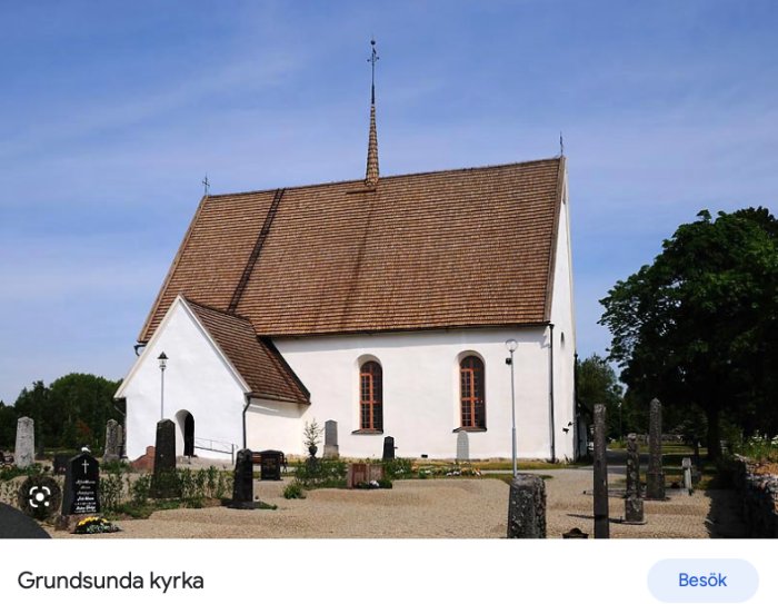 Vit kyrka med tegeltak, kyrkogård framför, klarblå himmel, gröna träd, solig dag.