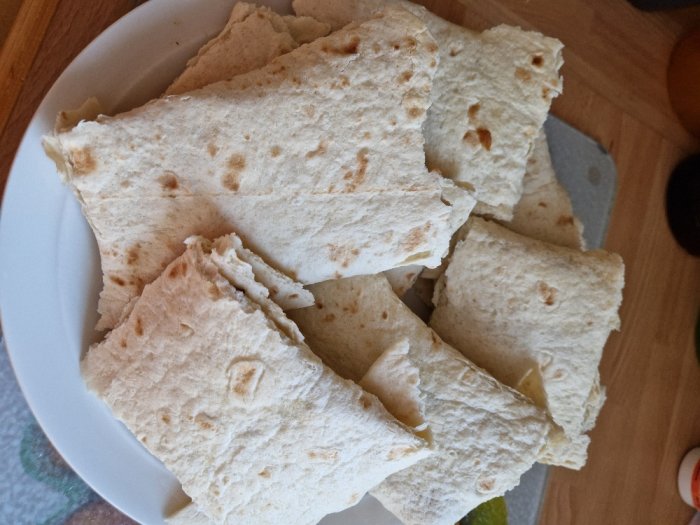 Vitt bröd, förmodligen tortillabröd, staplade på en vit tallrik, verkar ofyllda.