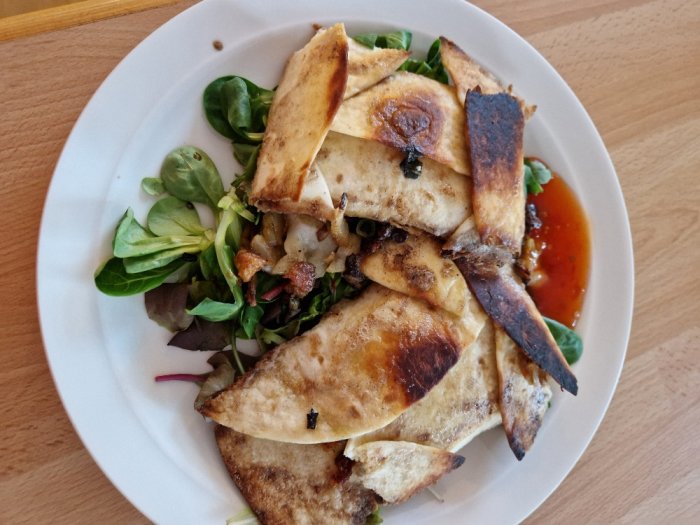 En tallrik med quesadilla, grönsallad och sås på en träbord.