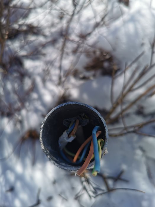 PVC-rör med kablar mot en snötäckt bakgrund, öppet och oskyddat, dagtid.